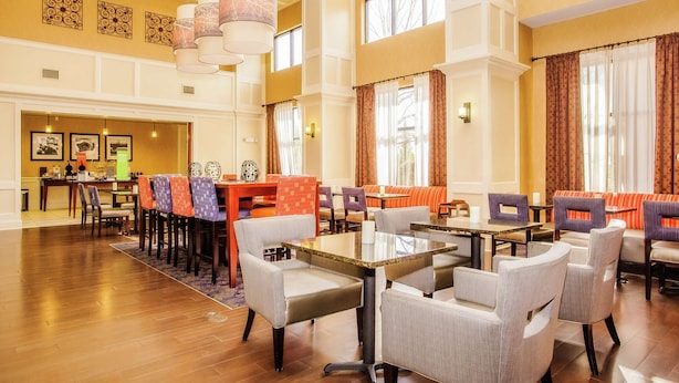 A spacious hotel lobby with multiple seating areas, including a dining table and chairs, and a reception desk. - Hampton Inn & Suites Sevierville @ Stadium Drive (Kodak)