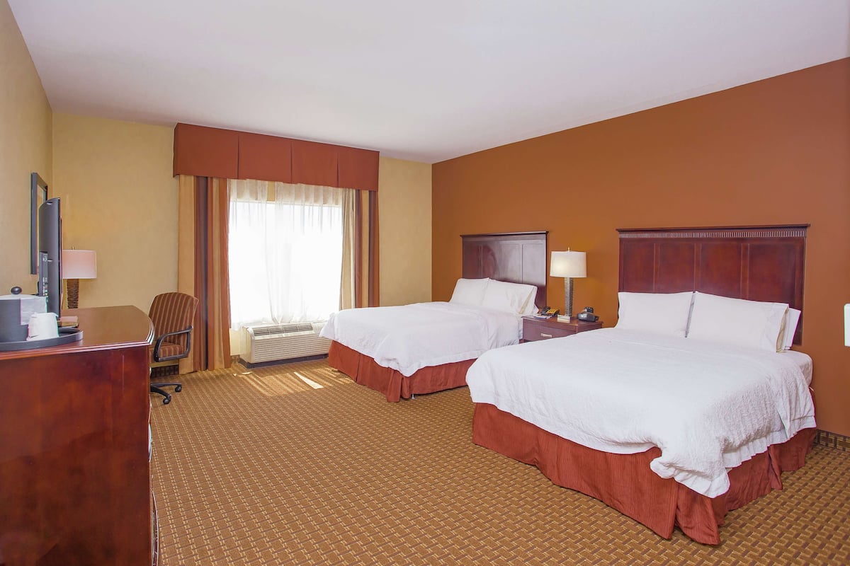 A hotel room with two beds, a desk, a chair, a nightstand, and a window with curtains.