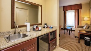 A hotel room with a kitchenette, a sink, a mirror, a dining area with a table and chairs, and a sofa. - Hampton Inn & Suites Sevierville @ Stadium Drive (Kodak)