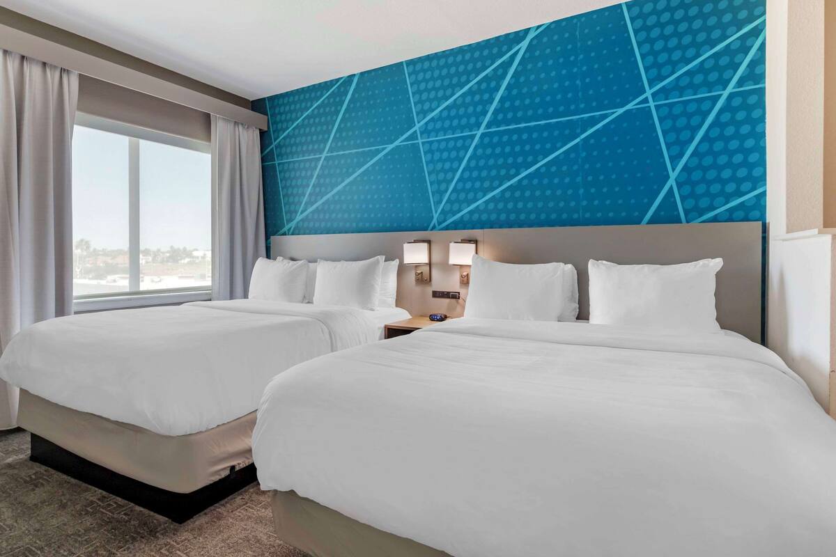 Ein Hotelzimmer mit zwei Betten, einem großen Fenster und einem blauen Wanddesign mit geometrischen Mustern.