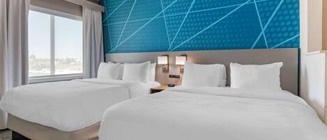 A hotel room with two beds, a large window, and a blue geometric wall design.