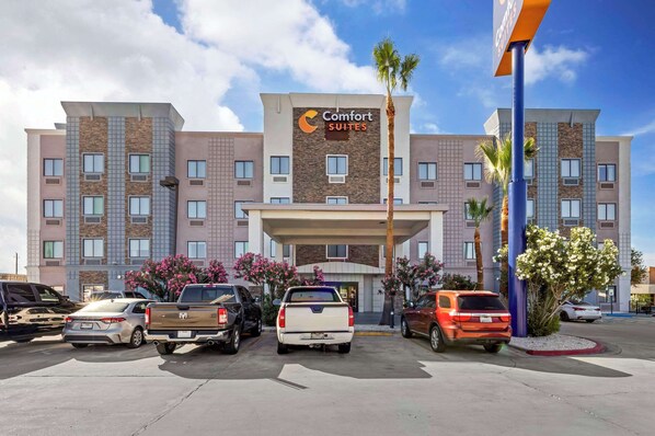 Un hotel Comfort Suites con una fachada moderna, varios espacios de estacionamiento y cielo despejado.