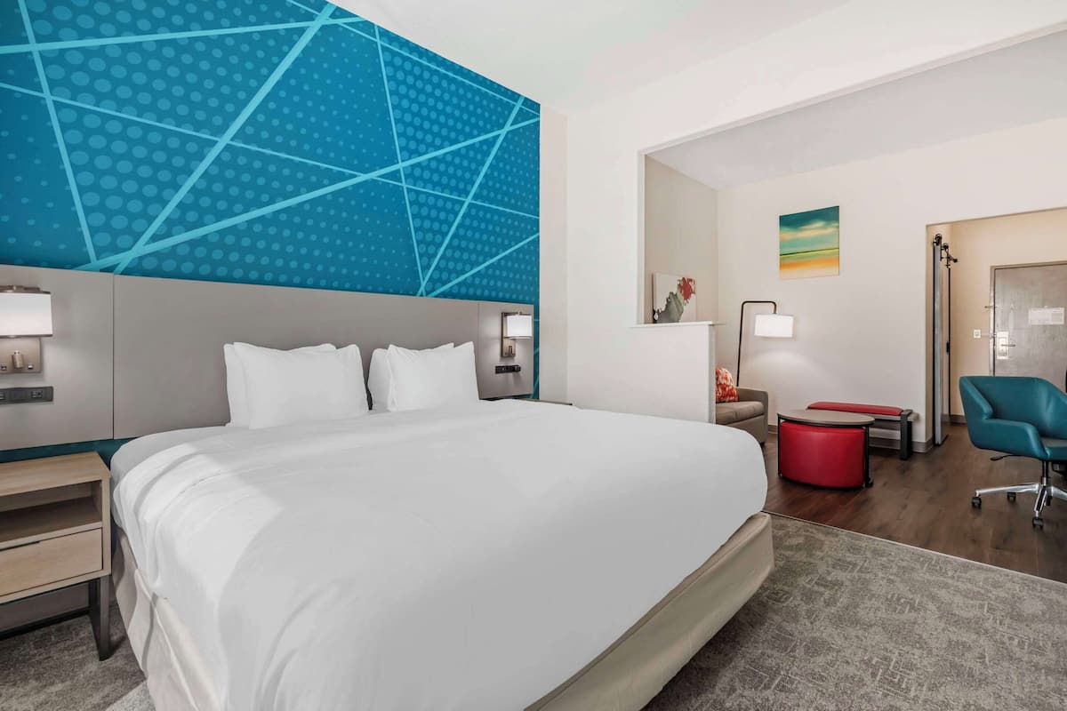 Ein modernes Hotelzimmer mit einem großen Bett, einem Schreibtisch, einem Stuhl und einem durchgegangenen Tür sichtbar erkennbaren Badezimmer.