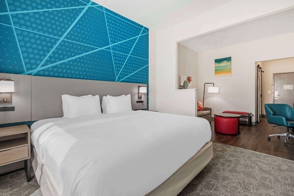 A modern hotel room with a large bed, a desk, a chair, and a bathroom visible through an open door.