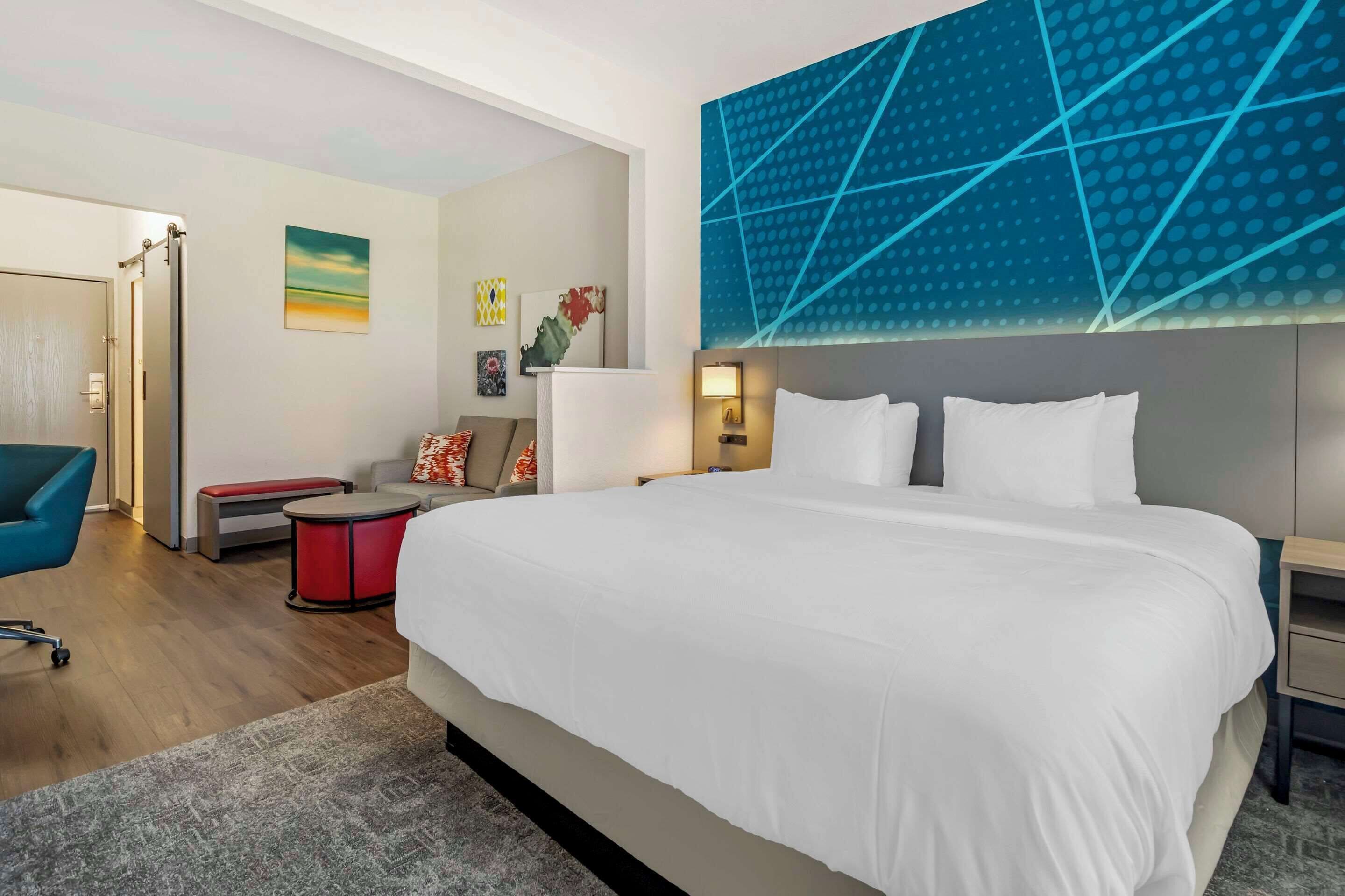 Quarto de hotel moderno com uma cama grande, uma escrivaninha, uma cadeira e um sofá.