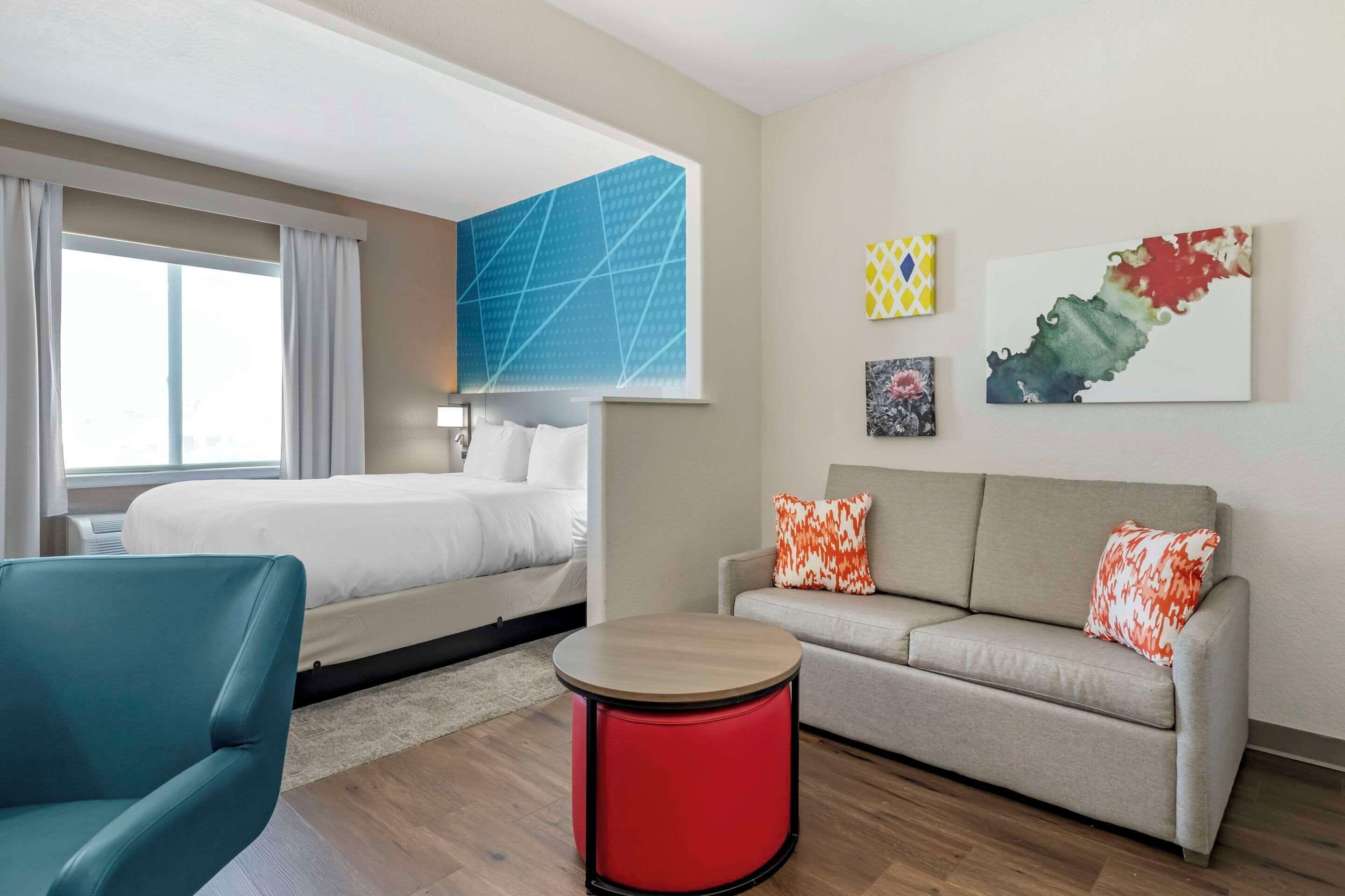 Une chambre d’hôtel avec un lit, un canapé, une table ronde rouge et des œuvres d’art accrochées au mur.