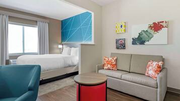 Une chambre d’hôtel avec un lit, un canapé, une table ronde rouge et des œuvres d’art accrochées au mur.