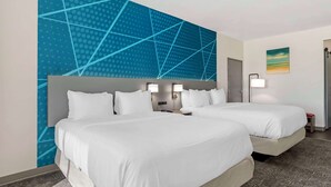 Ett hotellrum med två sängar, en stor, geometrisk väggmålning, en tavla och ett nattduksbord med en lampa.