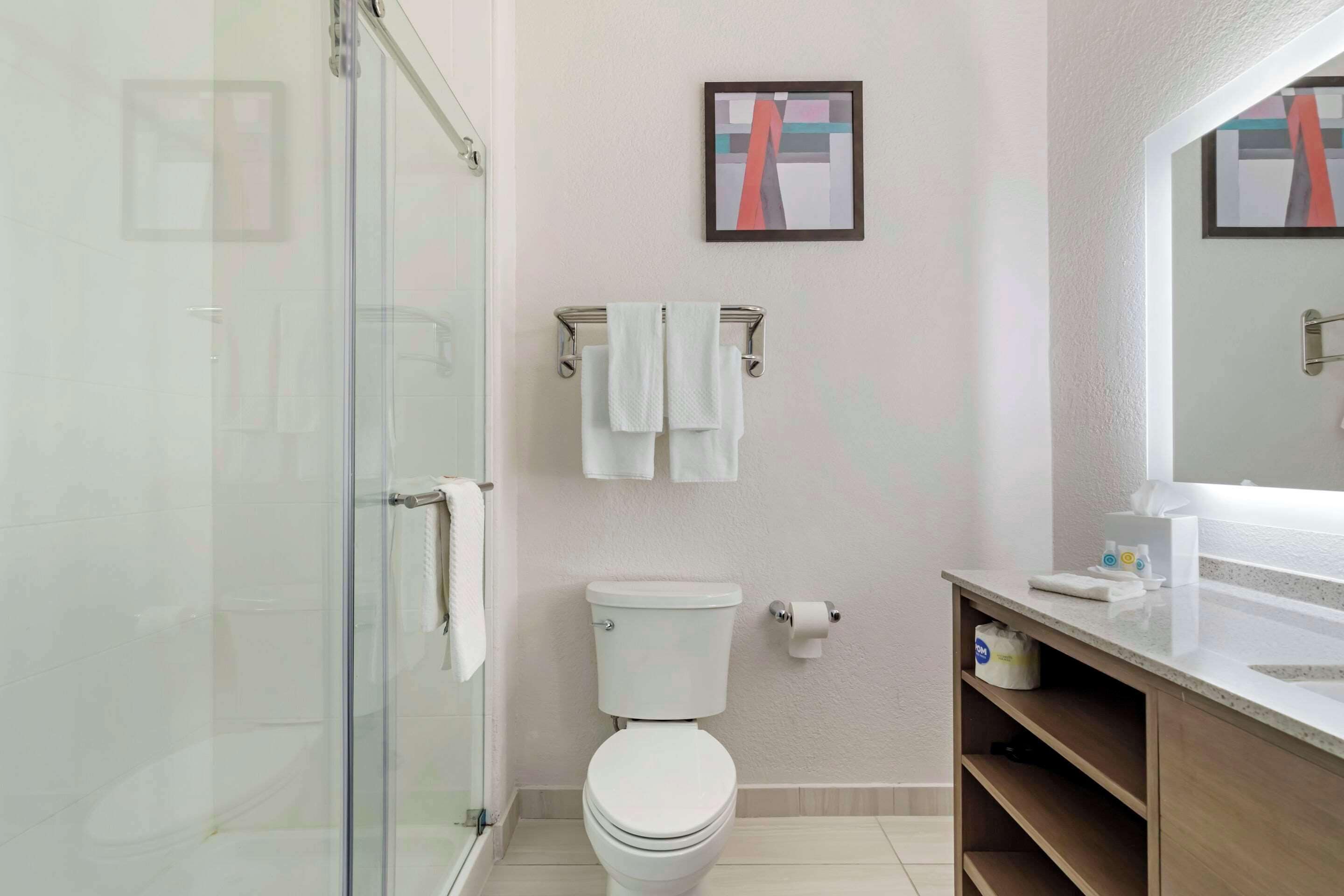 Une salle de bain moderne avec une douche à parois de verre, des toilettes, un lavabo avec un miroir et un porte-serviettes.