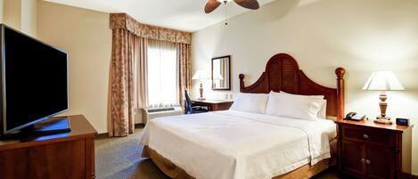 A hotel room with a bed, a television on a wooden cabinet, a desk with a lamp, and a ceiling fan.