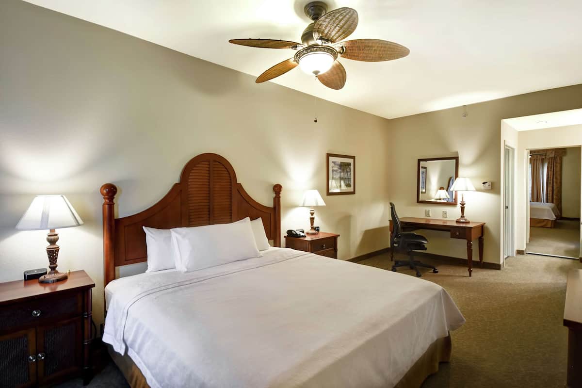 A hotel room with a large bed, a desk, a chair, a ceiling fan, and a mirror.