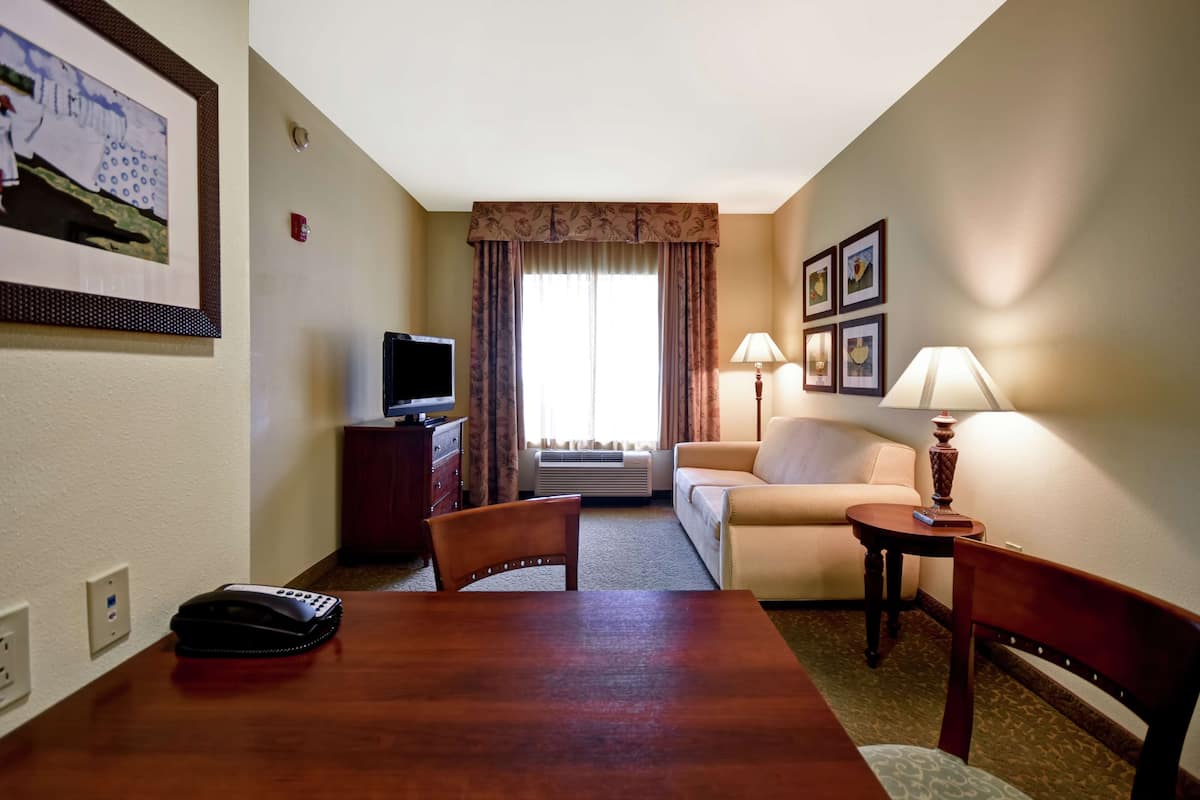 A hotel room with a wooden table, a sofa, a TV, and a lamp.