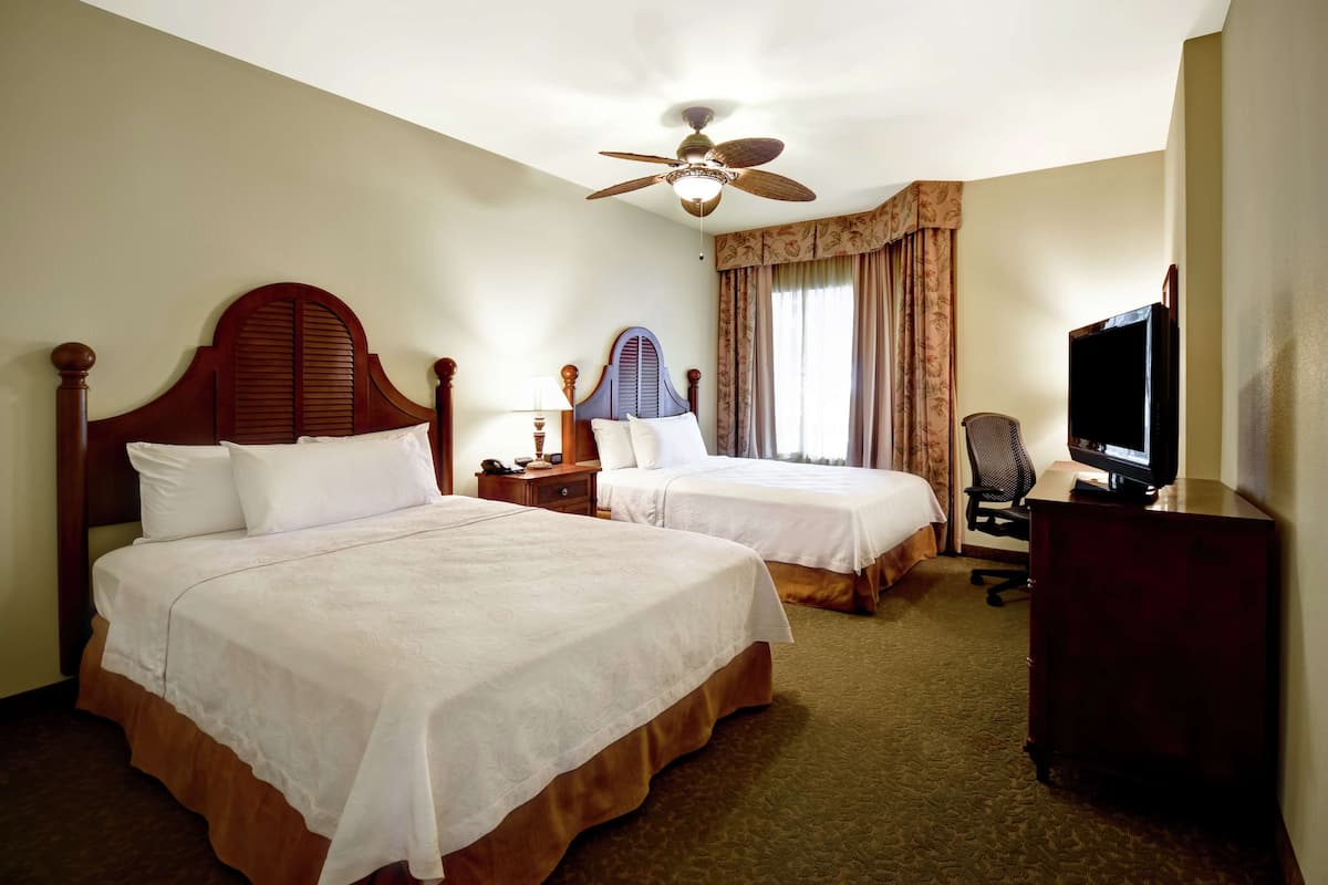 A hotel room with two beds, a ceiling fan, a TV, and a desk.