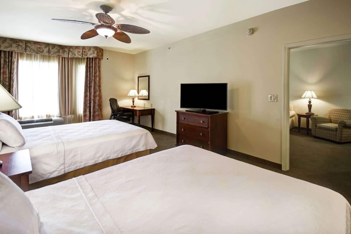A hotel room with two beds, a desk, a television, and a ceiling fan.