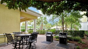 An outdoor patio with a brick floor, a round table with chairs, and a grill. - Homewood Suites by Hilton Charleston Airport (North Charleston)