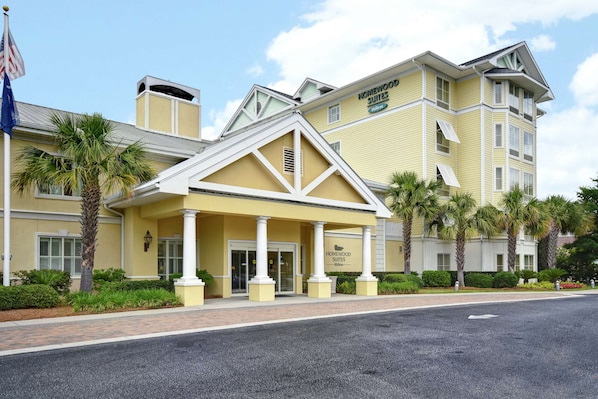 Un hotel con fachada amarilla, un acceso cubierto y palmeras.