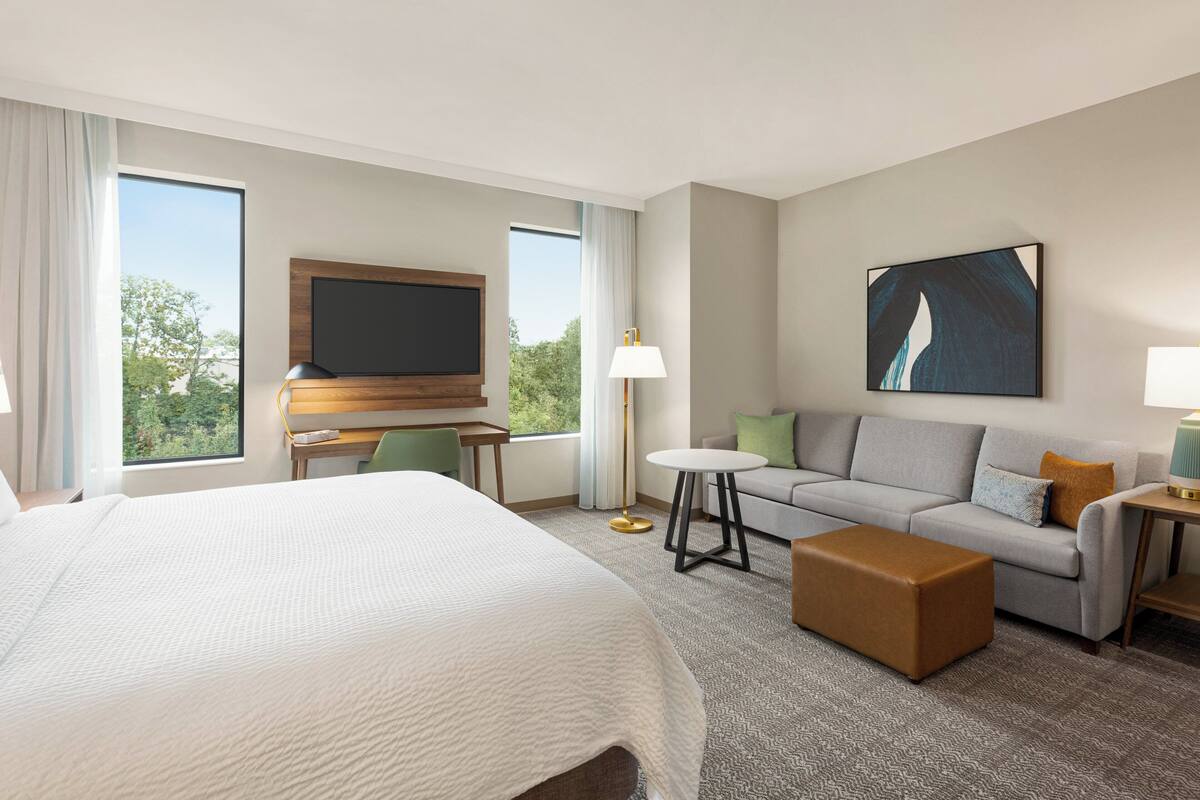 A hotel room with a large bed, a sofa, a small table, a TV, and a window with curtains.