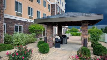 A covered outdoor area with a barbecue grill, surrounded by a landscaped garden with shrubs and flowers.