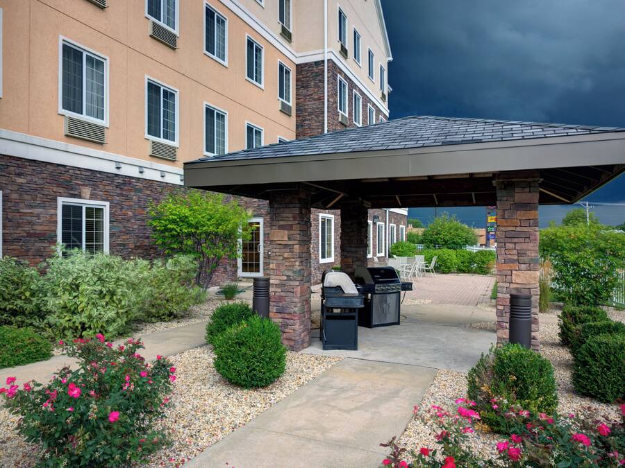A covered outdoor area with a barbecue grill, surrounded by a landscaped garden with shrubs and flowers.