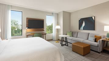 A hotel room with a large bed, a sofa, a coffee table, a TV, and a painting on the wall.