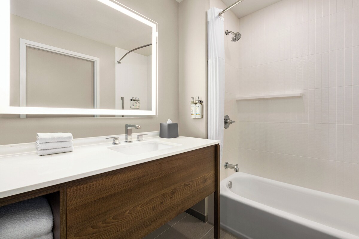 Een moderne badkamer met een houten wastafelmeubel, een grote spiegel, een bad en een douchegordijn.