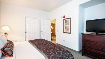 A hotel room with a bed, a TV, a dresser, and a door leading to another room.