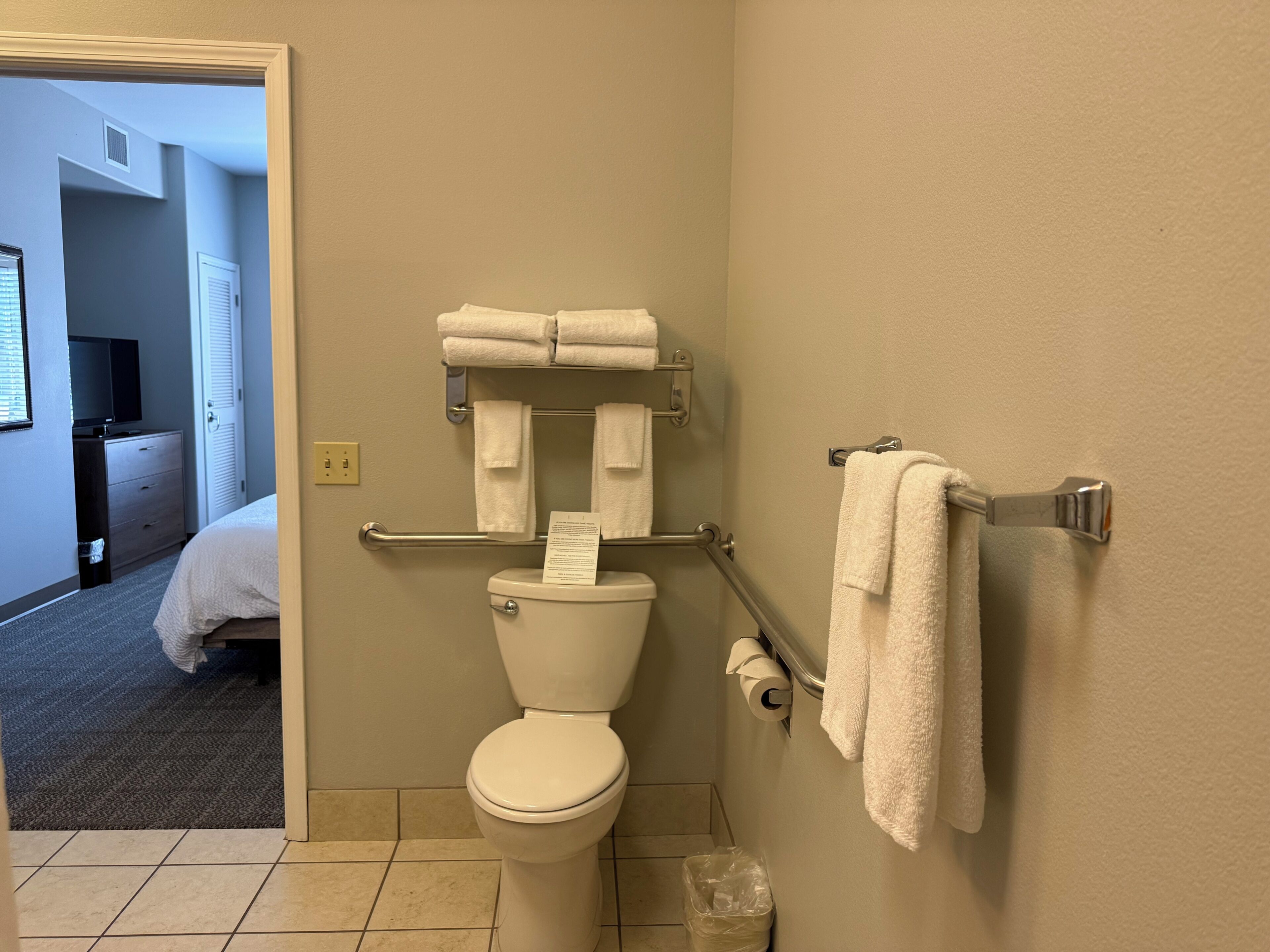 A bathroom with a toilet, towel rack, and a visible trash bin.