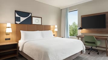 Una habitación de hotel con una cama grande, dos mesitas de noche con lámparas, un escritorio con una silla, un televisor de pantalla plana y obras de arte en la pared.