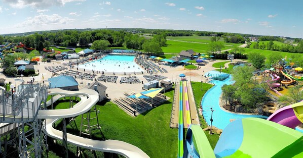 Een waterpark met meerdere glijbanen, een groot zwembad en een sportveld op de achtergrond.