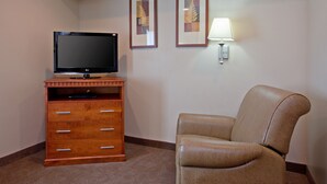 Une chambre d’hôtel équipée d’un téléviseur à écran plat posé sur un meuble en bois, d’une chaise et de deux tableaux encadrés accrochés au mur.