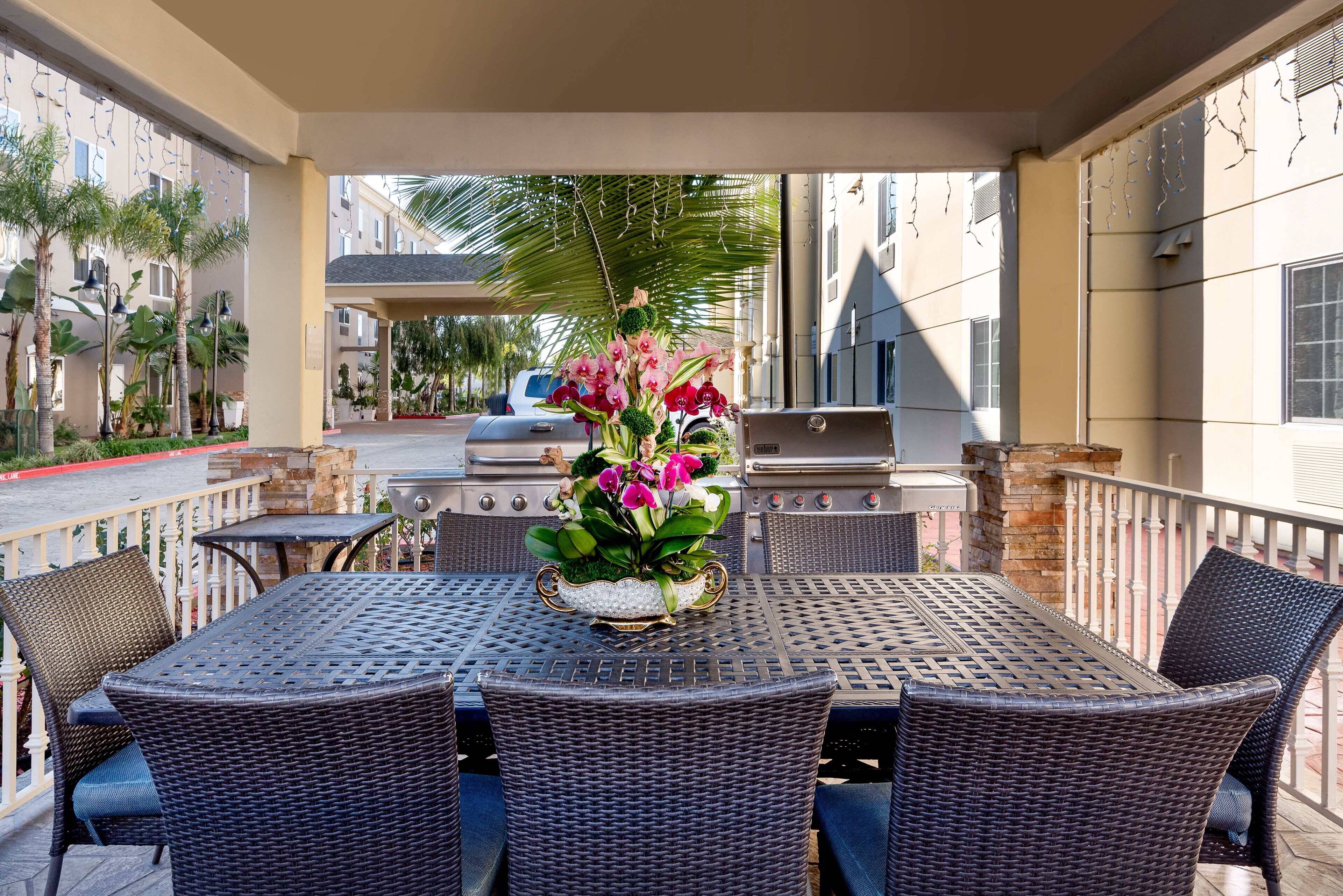 Un patio al aire libre con una parrilla, mobiliario de mimbre y un arreglo floral.