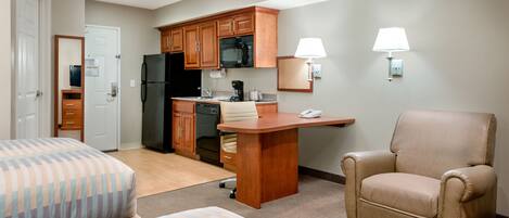 Una habitación de hotel compacta con dos camas, una kitchenette, un escritorio y una silla.