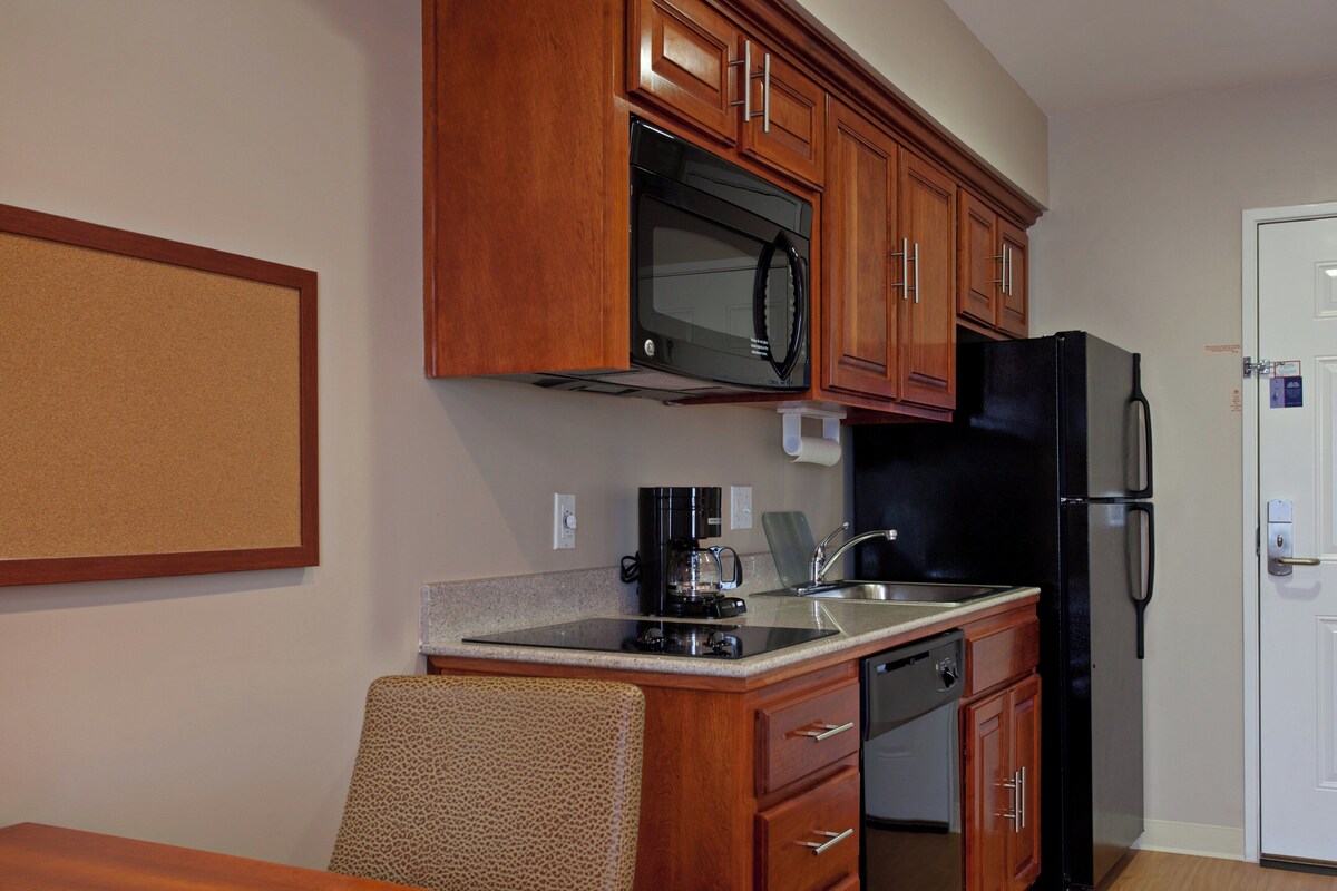 A compact kitchen with wooden cabinets, a microwave, a refrigerator, a coffee maker, and a dishwasher.
