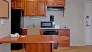 Een functionele keuken met houten kastjes, een magnetron, een koffiezetapparaat en een eettafel met stoelen.
