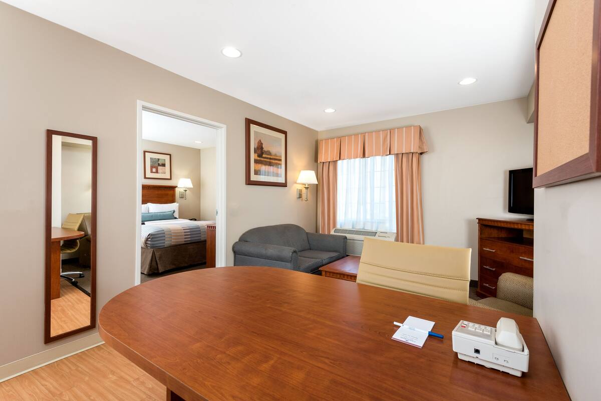 Een hotelkamer met een houten bureau, een bank, een bed, een televisie en een raam met gordijnen.