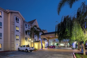 A hotel entrance with a covered walkway, a parking area, and a red vehicle parked in front.