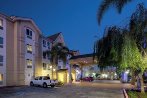 A hotel entrance with a covered walkway, a parking area, and a red vehicle parked in front.