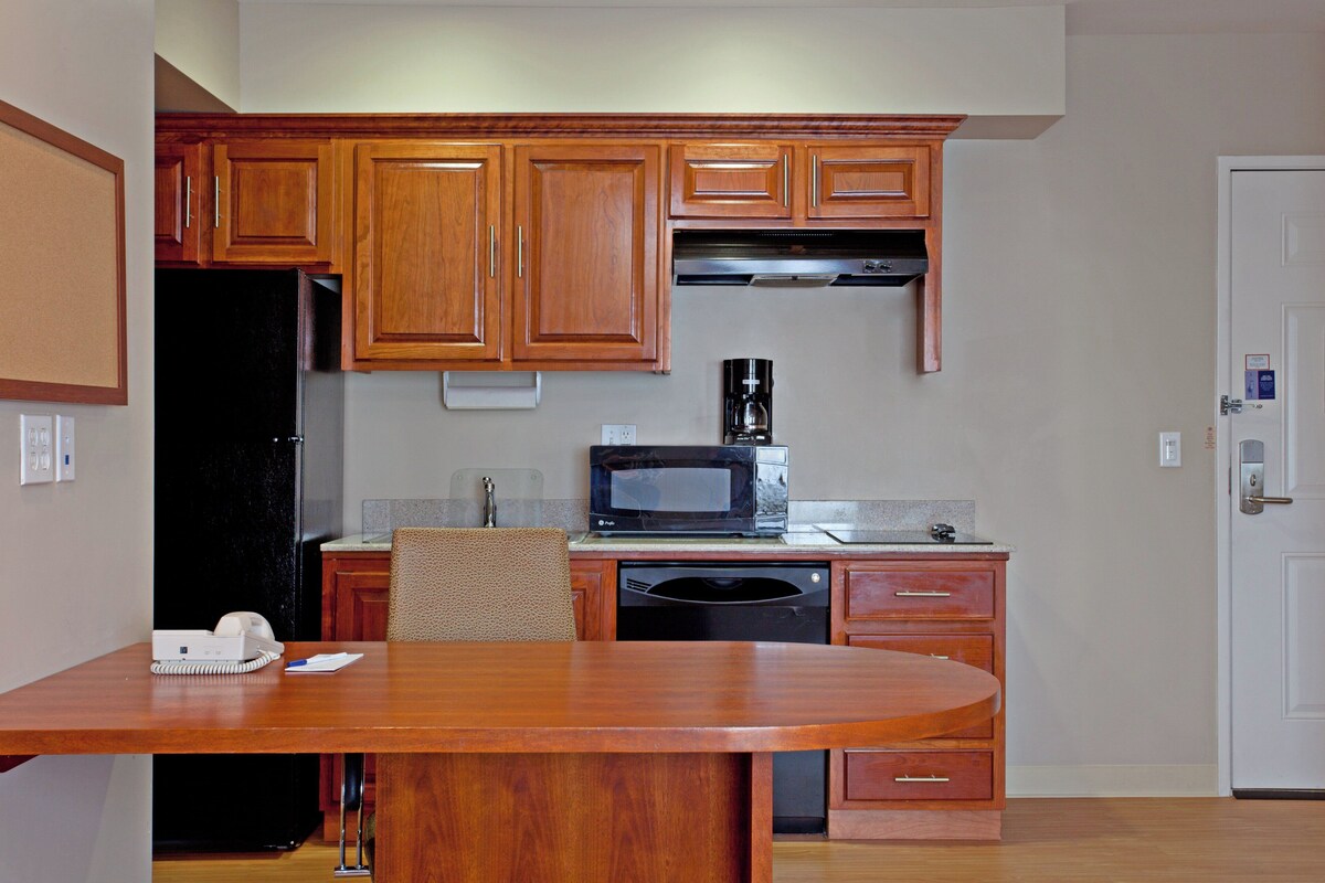 A compact kitchen with wooden cabinets, a microwave, a coffee maker, and a dining table with chairs.