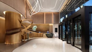 A modern hotel lobby with a curved reception desk, a large woven sculpture, and a contemporary ceiling design.