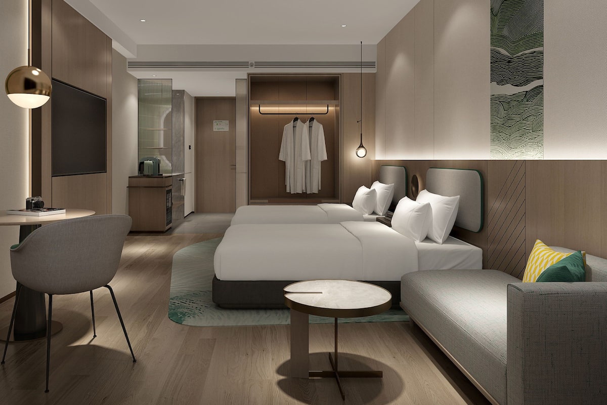 A modern hotel room with a large bed, a sofa, a desk, and a chair.