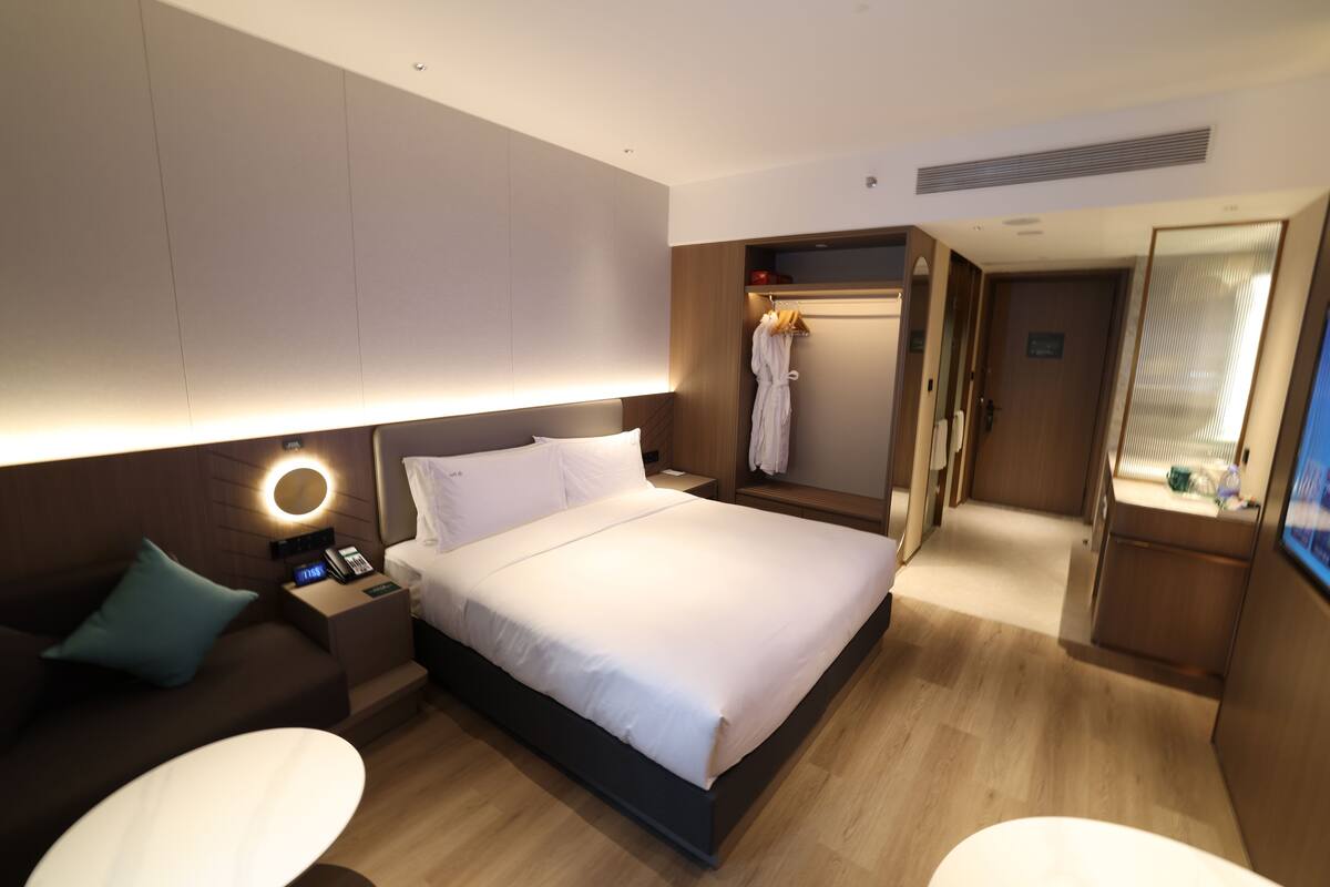 A modern hotel room with a large bed, bedside tables, a desk, and a walk-in closet.