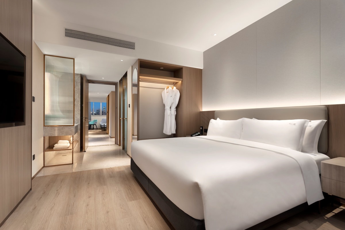 Une chambre d’hôtel moderne dotée d’un grand lit, d’un dressing et offrant une vue sur la ville.