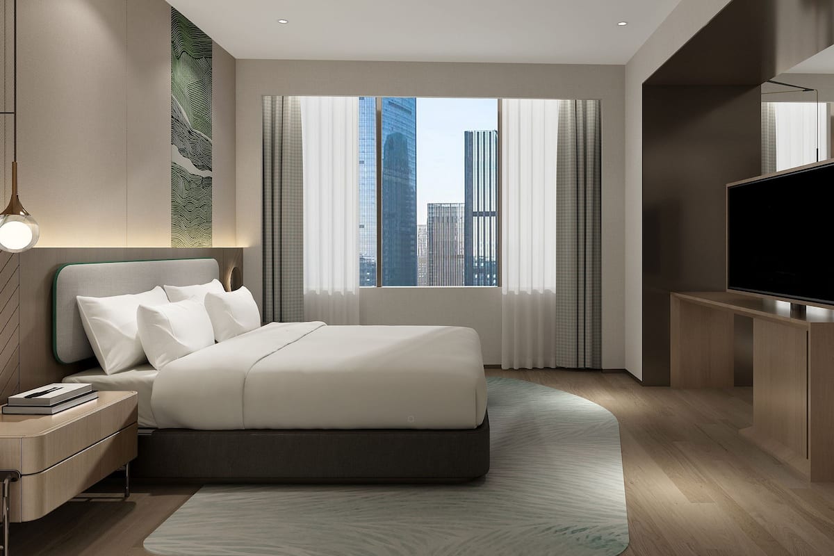 A modern hotel room with a large bed, a desk, a flat-screen TV, and a city view.