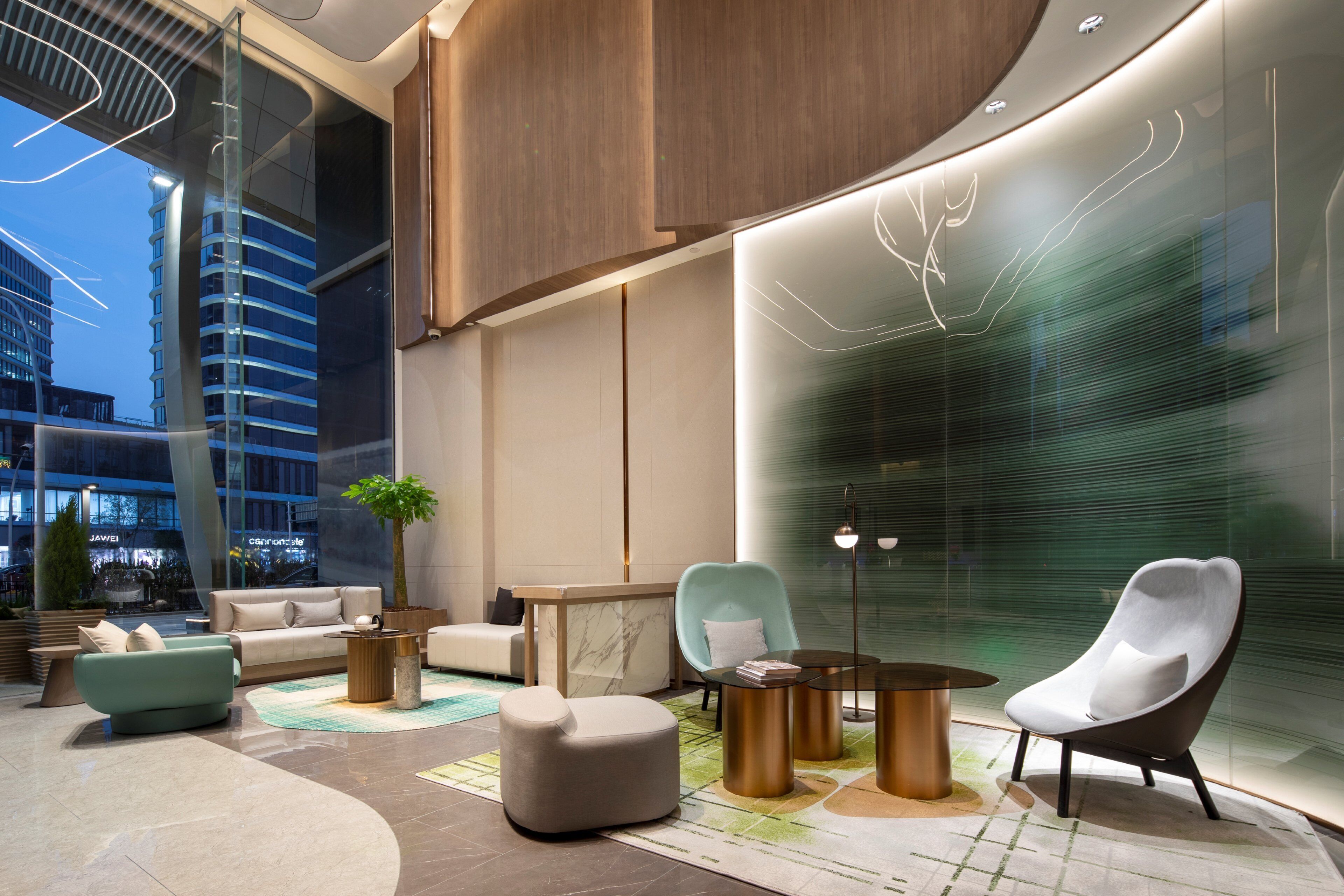 A modern lobby with a curved ceiling, a seating area with sofas and chairs, a coffee table, and a large window offering a view of the cityscape.