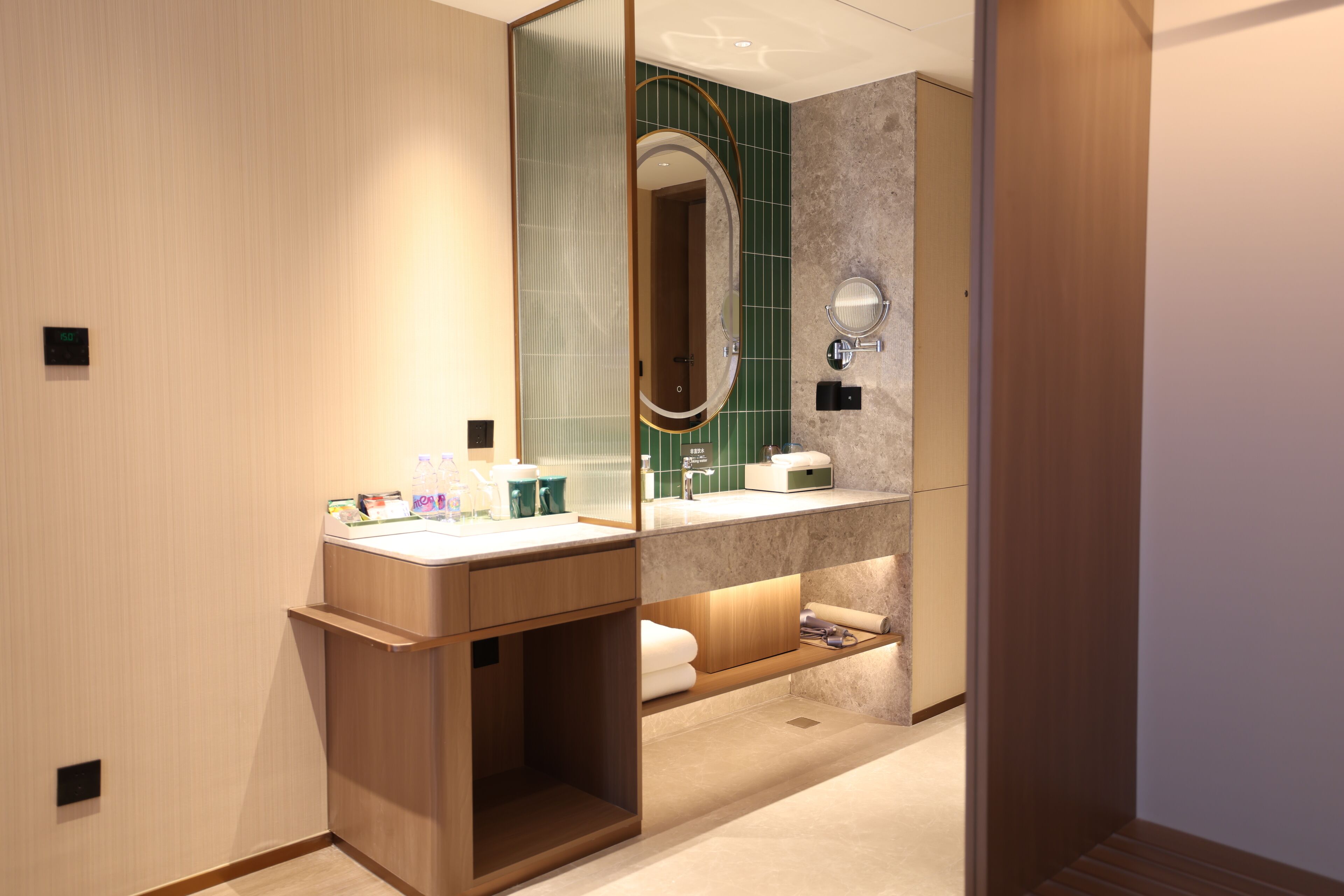 A modern bathroom with a wooden vanity, a large mirror, and a green-tiled shower area.