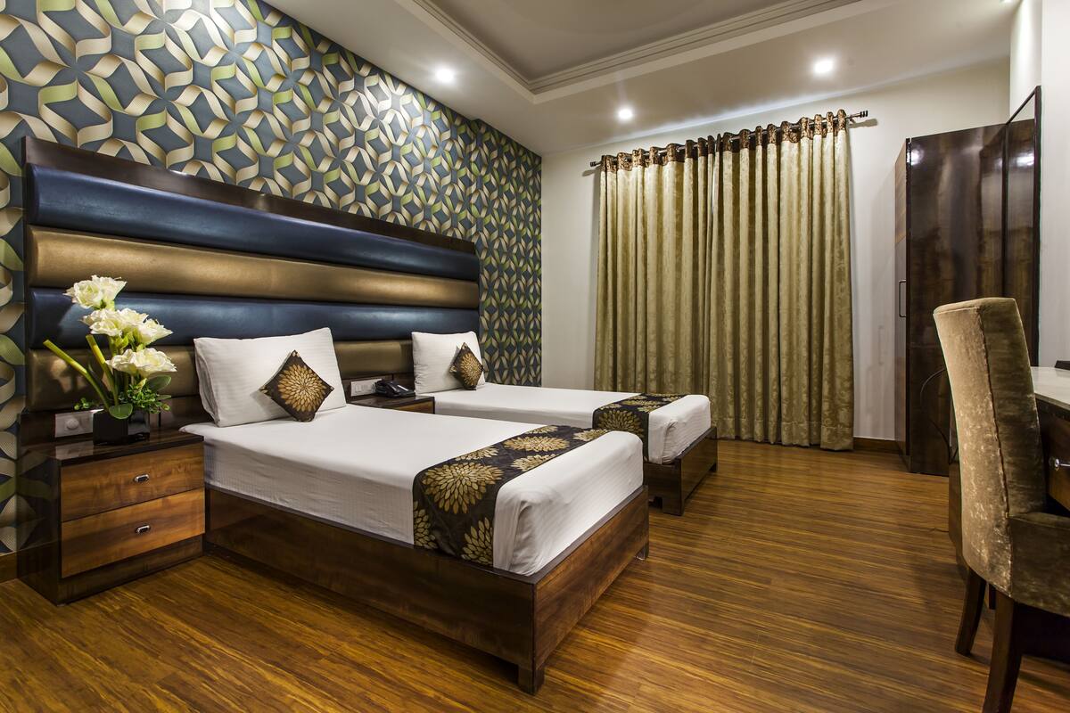 Habitación de hotel con dos camas, piso de madera, pared con diseño y cortina.
