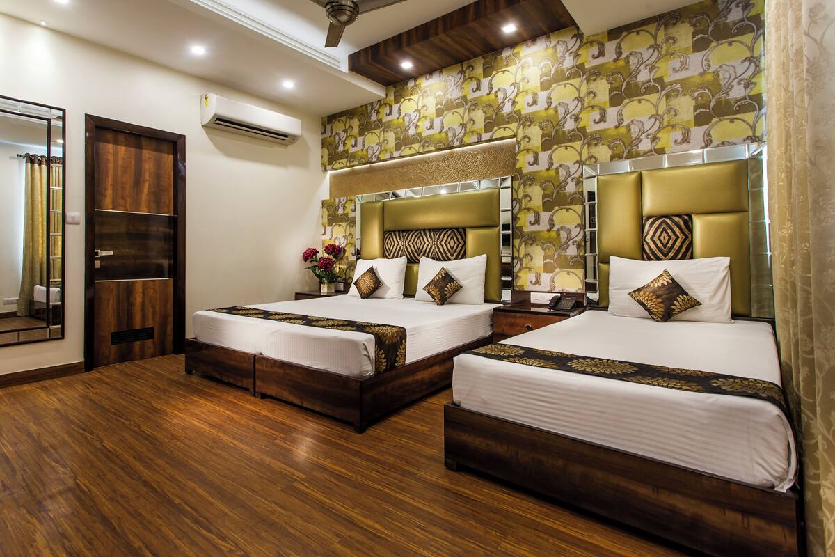 Habitación de hotel con dos camas, suelo de madera, un espejo grande y papel tapiz estampado.