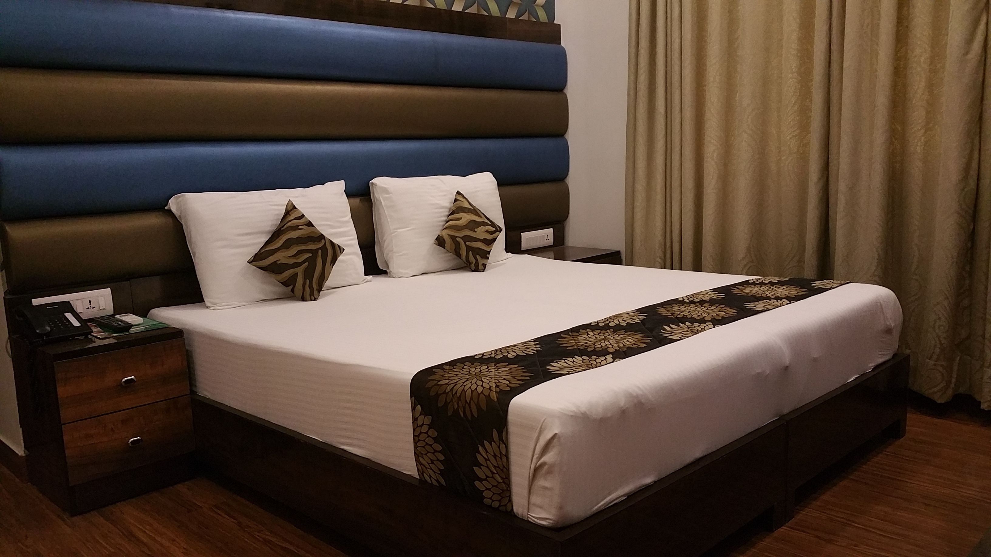 A hotel room with a large bed, a wooden nightstand, a desk, and a brown headboard.