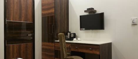 Habitación de hotel con armario, escritorio, silla, televisión y cafetera.