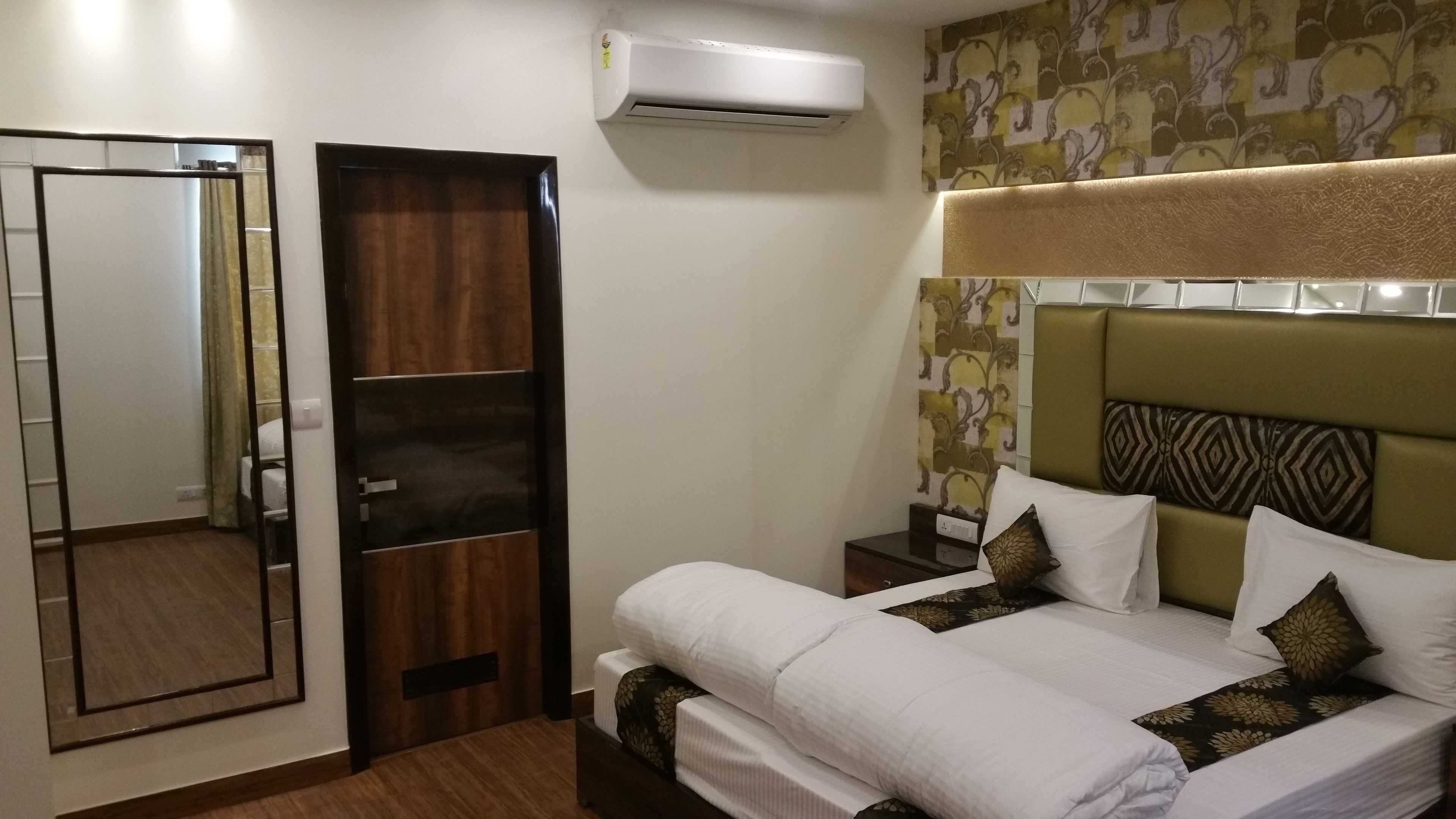 A hotel room with a bed, a wardrobe, a mirror, and an air conditioning unit.